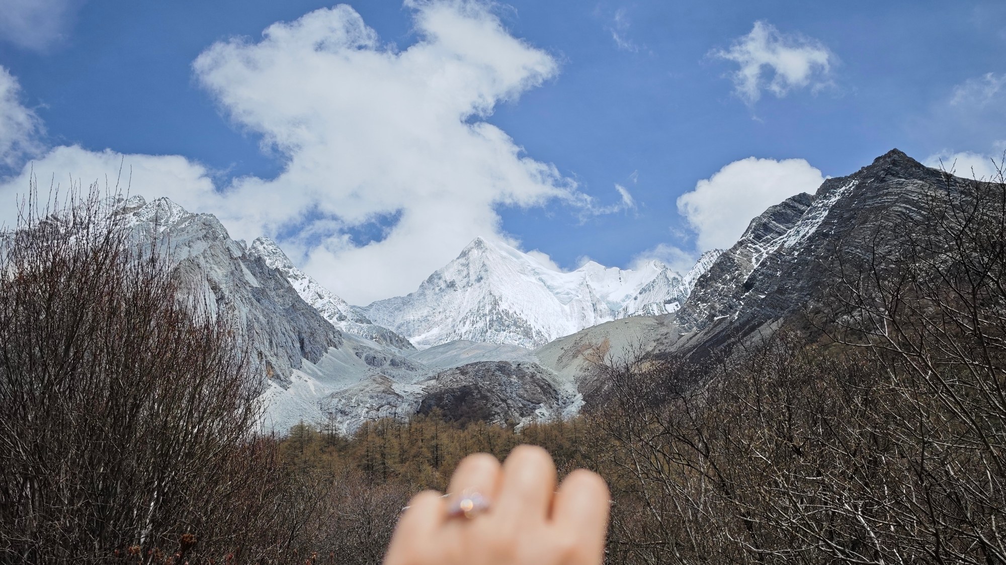 稻城亚丁的求婚纪念：戴着戒指的手伸向镜头，远处是蓝天下的雪山